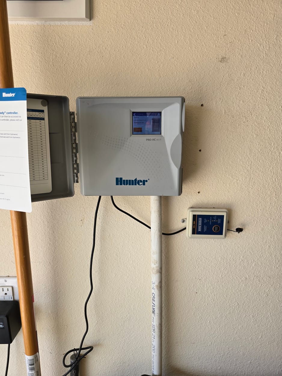 Wall-mounted lawn irrigation controller with its cover open for operation checks, documented on a North Texas inspection
