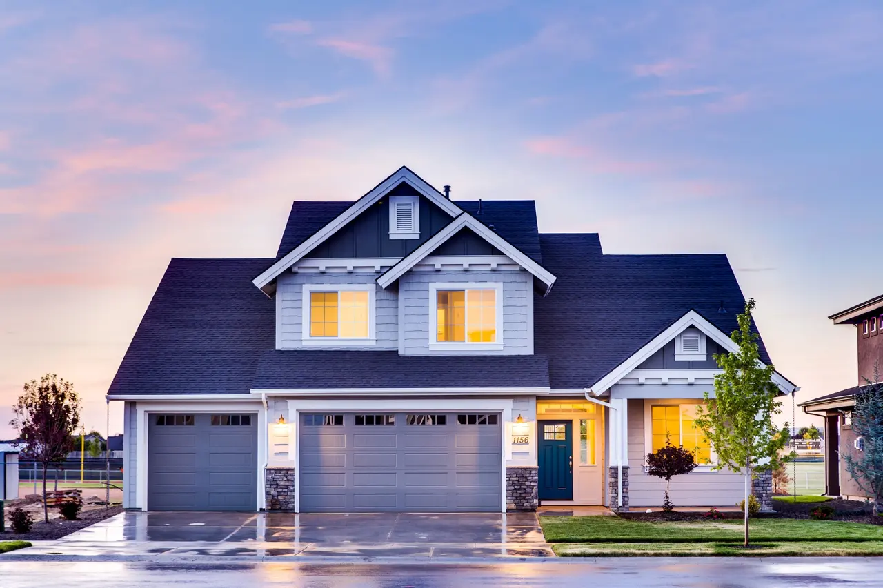 Newly built two-story home with a three-car garage and lit windows at dusk